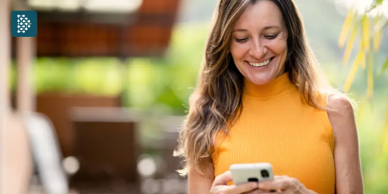 mulher loira vestindo camiseta amarela usa celular para fazer agendamento de consulta por meio de sistema de automação para clínicas