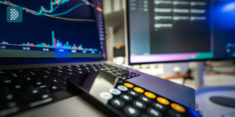Computador exibindo gráficos financeiros e celular com calculadora, representando o controle financeiro hospitalar com o sistema Datasigh Web.