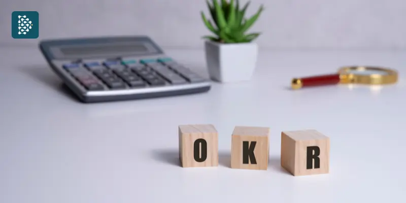 dados de madeira com as letras okr ao lado de um calculadora e uma planta suculenta