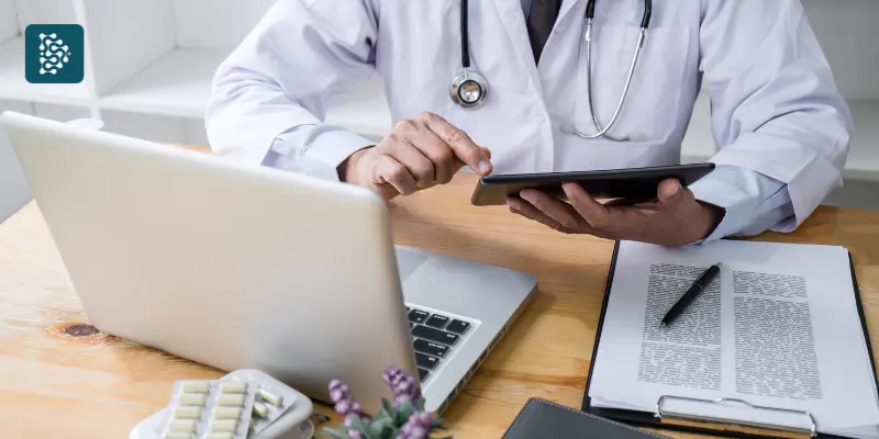 médico, usando um tablet enquanto está sentado em uma mesa de trabalho.