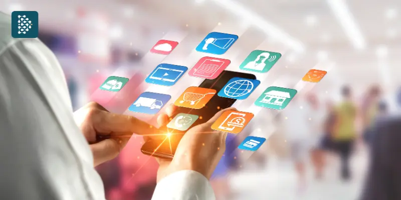 Mão segurando smartphone com ícones de aplicativos de comunicação digital.