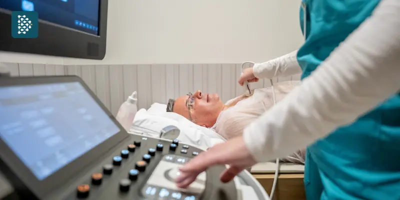 Enfermeira realiza ecocardiograma em homem deitado na maca durante exame médico em clínica de cardiologia.