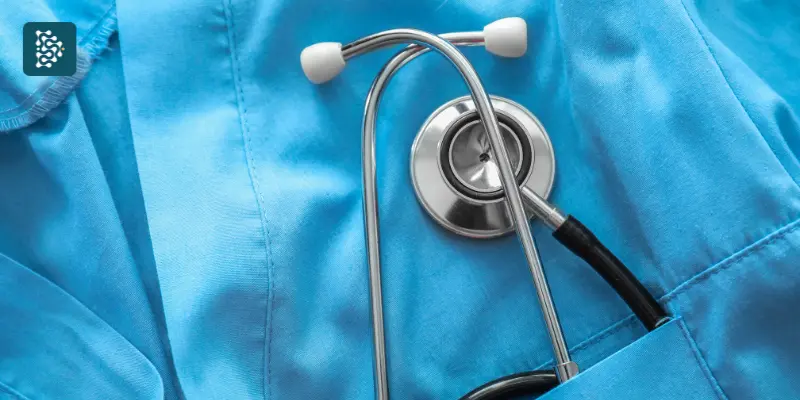 Estetoscópio médico repousa sobre um uniforme de hospital azul, simbolizando Excelência Organizacional no setor de saúde. A imagem transmite profissionalismo, cuidado e eficiência na área médica.