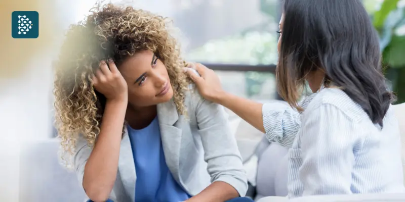 Mulher fala sobre saúde mental enquanto coloca as mãos no ombro da amiga.