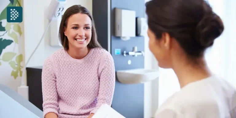 Paciente sorridente conversa com profissional de saúde em consultório moderno, mostrando confiança e atendimento humanizado na Jornada do Paciente