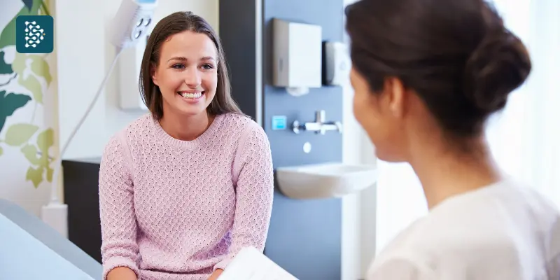 Paciente sorridente conversa com profissional de saúde em consultório moderno, mostrando confiança e atendimento humanizado na Jornada do Paciente