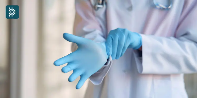 Médica de jaleco branco colocando luvas de borracha antes de atendimento clínico.