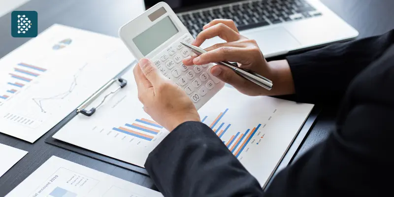 mãos de uma pessoa usando computador e calculadora para calcular ROI da compra de software para área médica