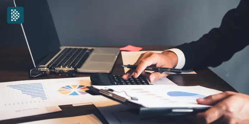 mãos de uma pessoa usando computador e calculadora para calcular ROI da compra de software para área médica