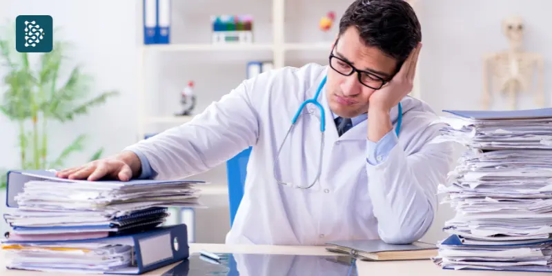 Médico frustrado diante de pilhas de papéis de consultório, simbolizando a falta de organização na clínica e a necessidade de gestão eficiente com o sistema hospitalar Datasigh.