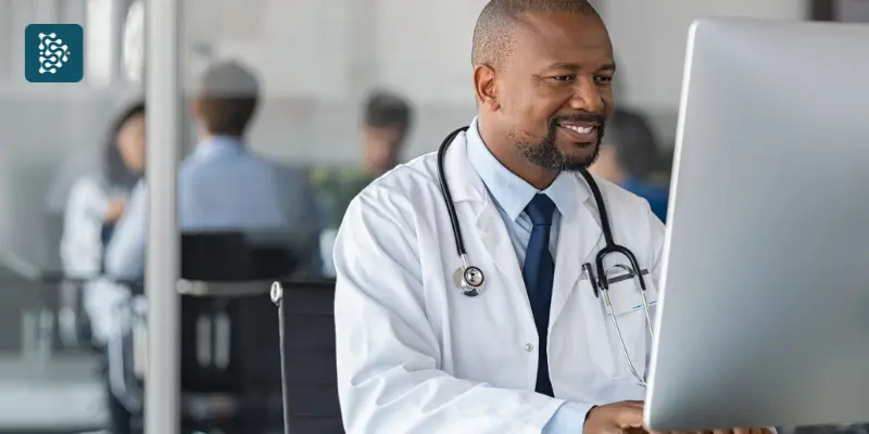 médico negro sorrindo com soluções digitais para hospitais olhando prontuário online em um computador