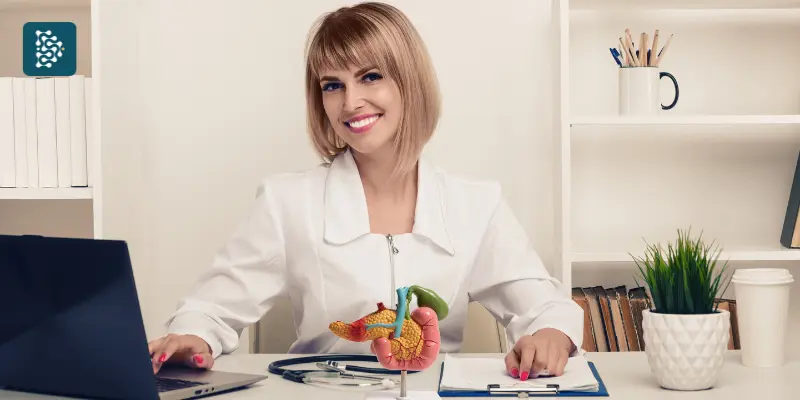médica gastroenterologista sorri feliz com a maquete de um estômago em frente a um computador com o software de gestão hospitalar datasigh