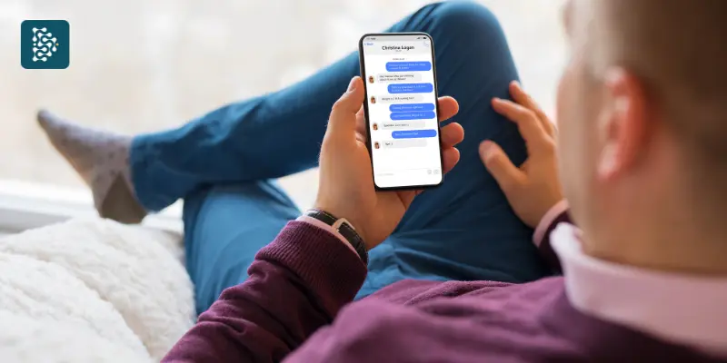Homem sentado no sofá lendo mensagens automáticas no WhatsApp com chatbot e automação de atendimento.