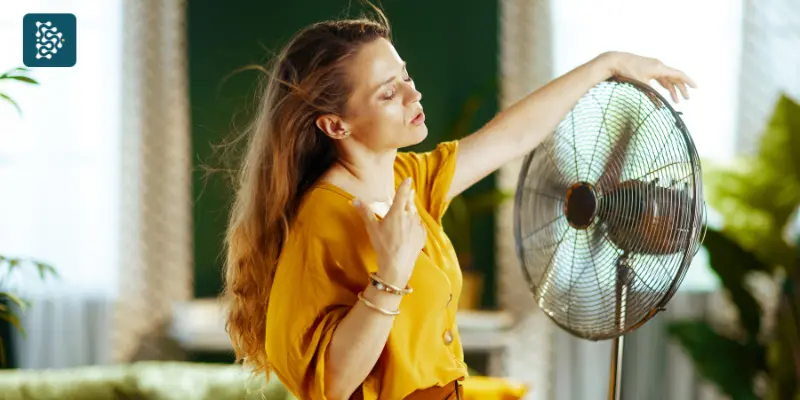 mulher com calor se refrescando na frente de um ventilador
