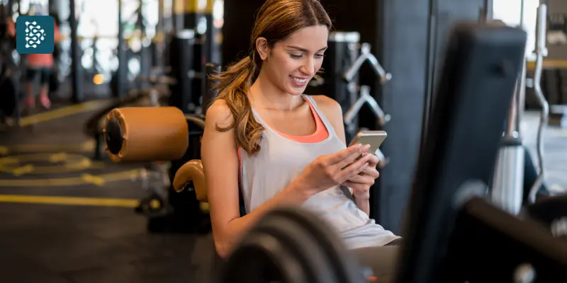 mulher sorrindo na academia com um celular na mão