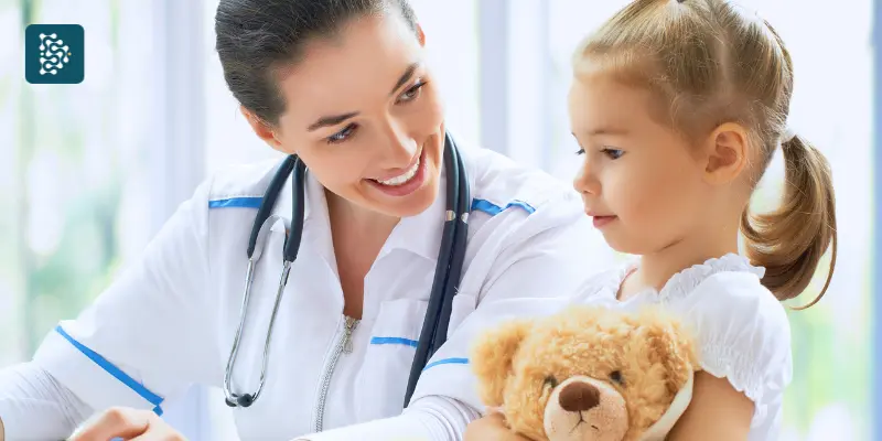 pediatra conversando com menina loira que segura um teddy bear