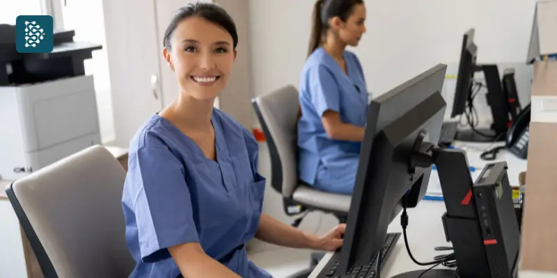 Recepcionista de clínica sorri enquanto usa o computador, satisfeita com o sistema DataSIGH de automação de processos em hospitais e clínicas.