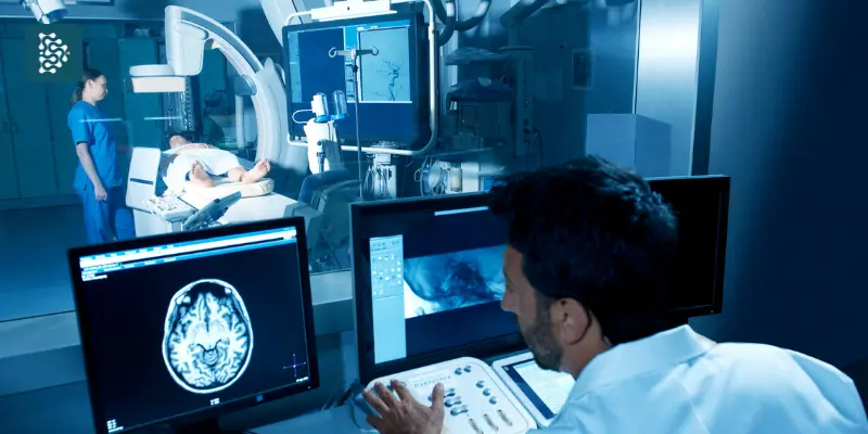 Profissional da saúde analisa imagens cerebrais em sistema digital enquanto paciente é examinado por equipe médica em sala de diagnóstico por imagem.
