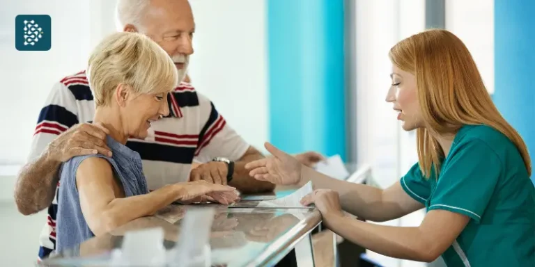 Recepcionista atende casal de idosos com agilidade usando sistema de gestão hospitalar em ambiente moderno e otimizado.