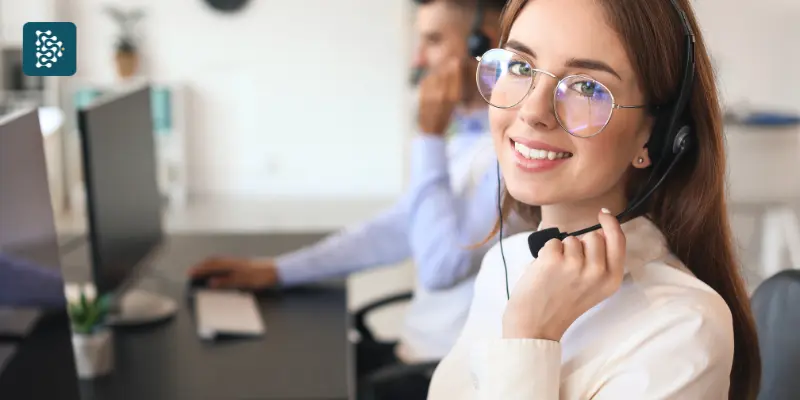 Mulher jovem de óculos redondos e uniforme branco com fone de ouvido, representando o suporte técnico e atendimento ao cliente do sistema hospitalar Datasigh para clínicas e hospitais.